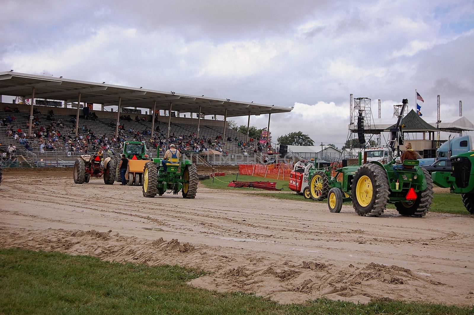 This is a group of tractor's awaiting there turn during a tractor pull at a county fair.