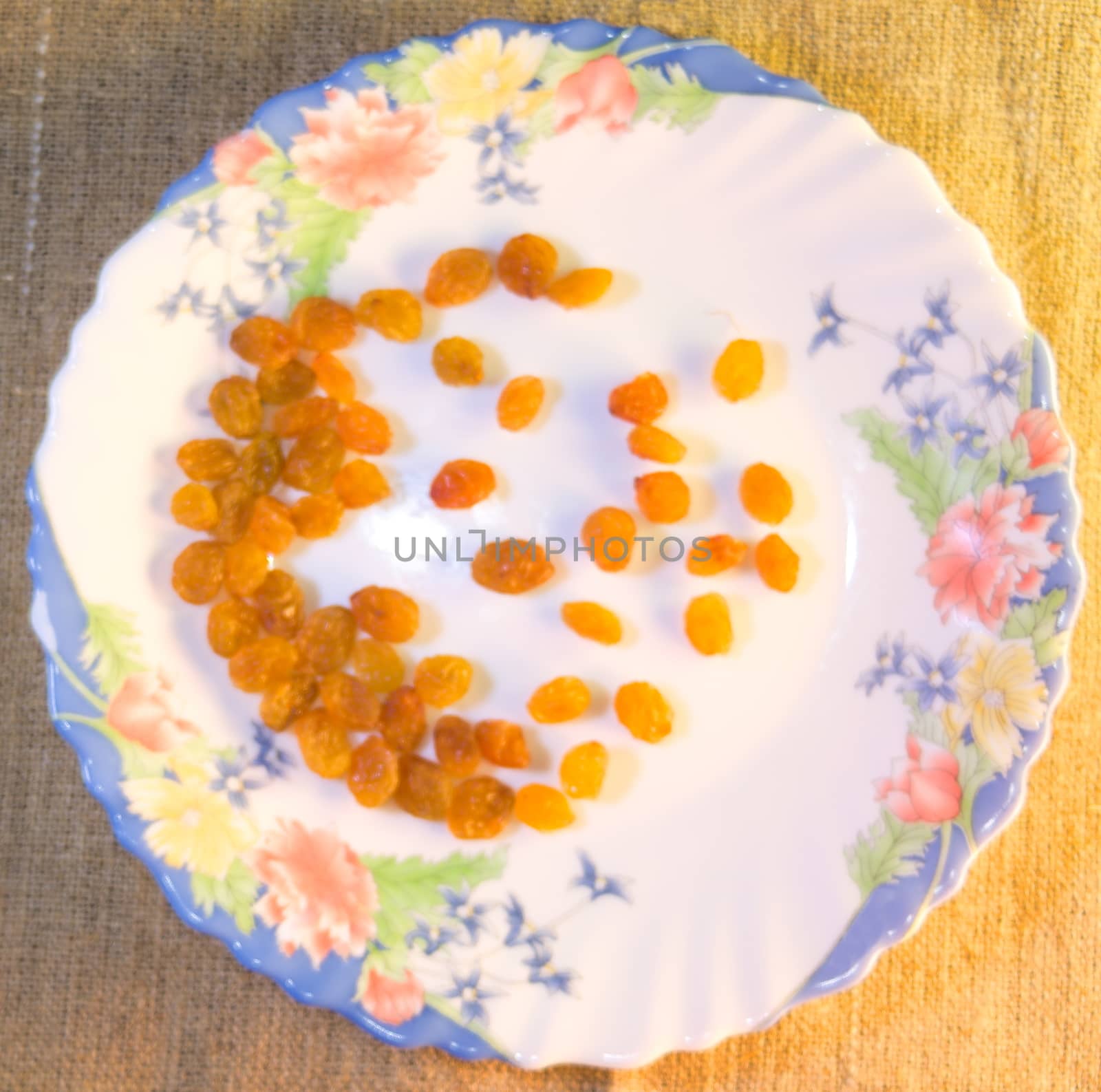 light yellow raisins are scattered on a beautiful white plate decorated with flowers