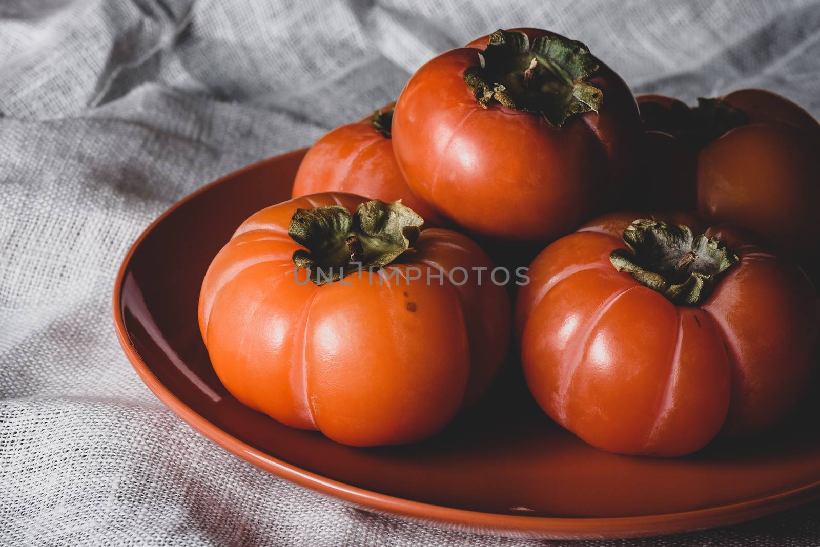 Few fresh persimmons on orange plate over white textile