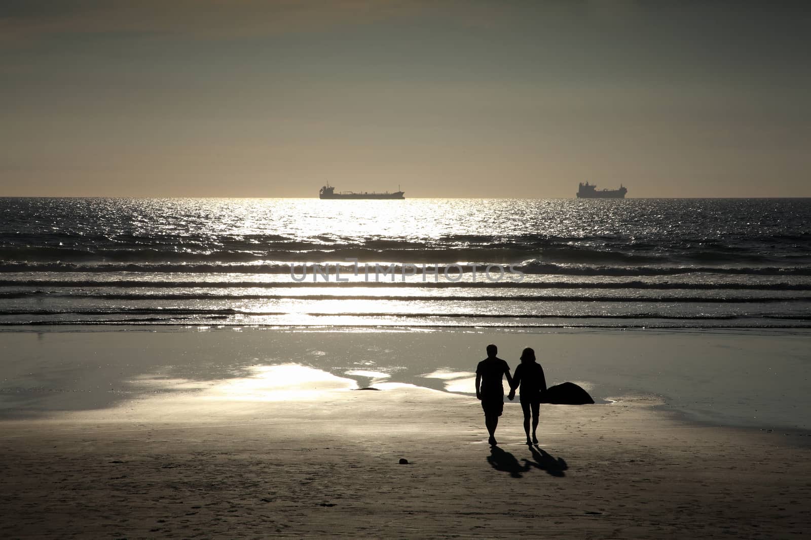 Couple lovers romantically walking in love on a silhouette sunset beach at Broad Haven Wales UK  a popular Welsh travel destination visitors resort stock photo