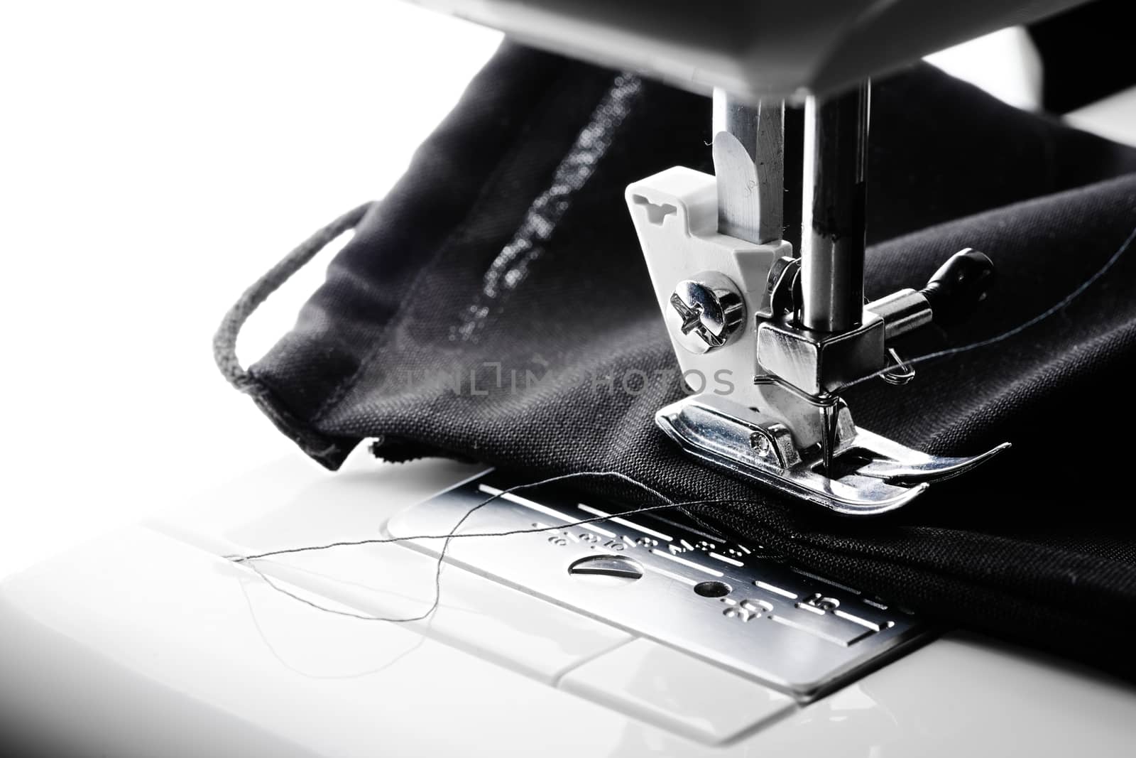 An all black face covering is stitched in a sewing machine. Blank white copy space to the left hand side. Contrasty image.