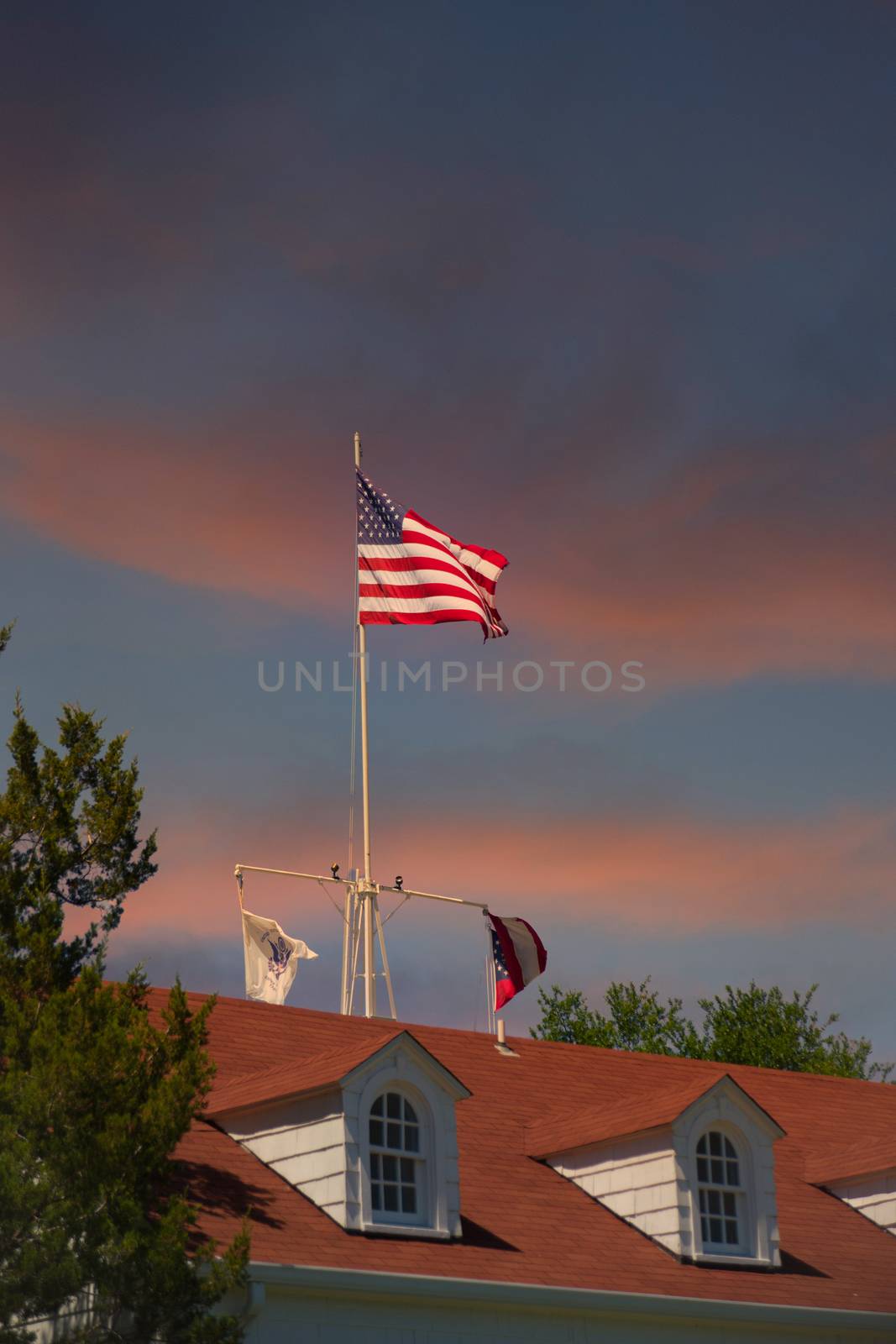 The American flag flying against a clear blue sky over a red roof with dormers