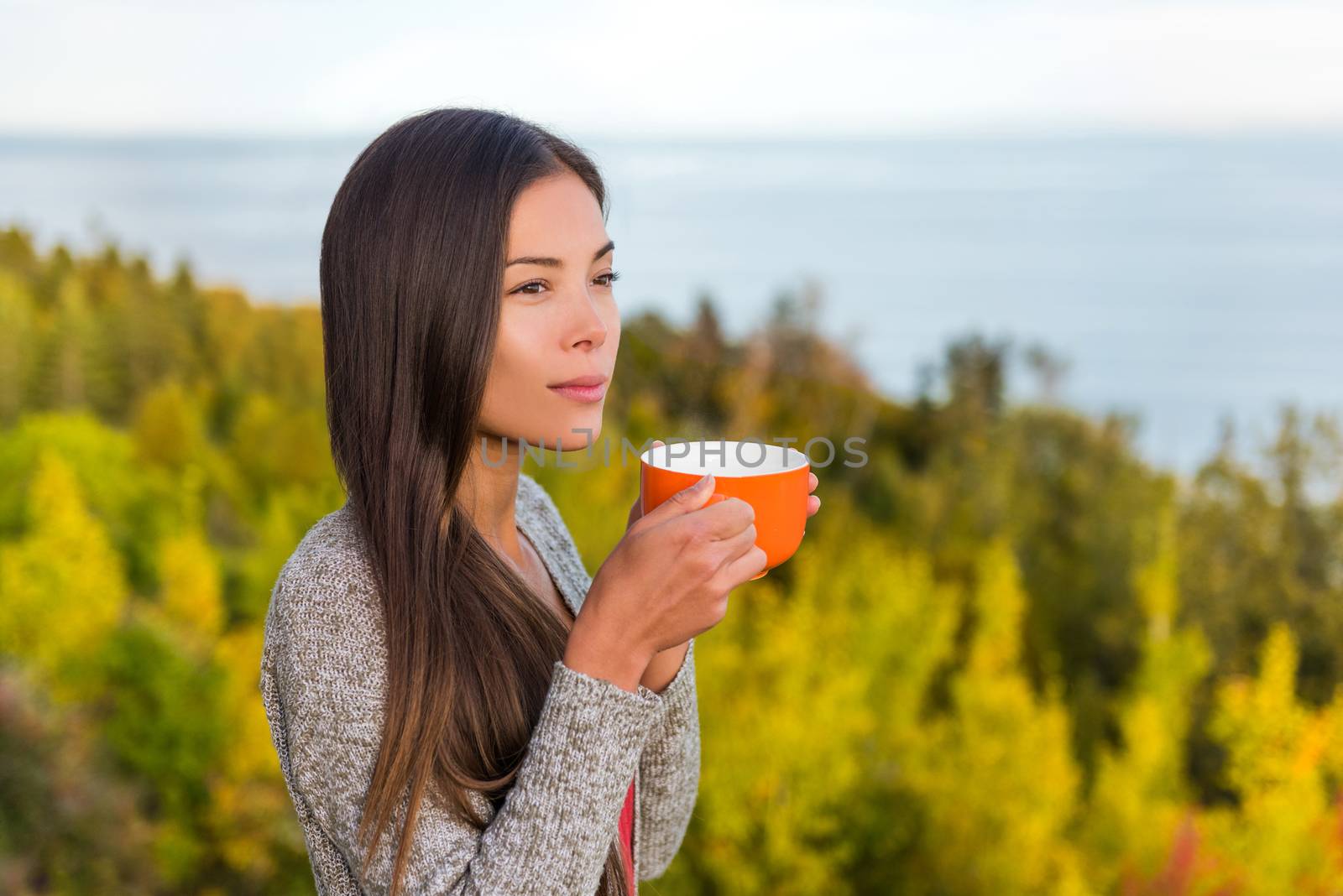 Nature outdoors coffee drinking woman relaxing in forest autumn sunshine enjoying her morning coffee. Happy multiracial canadian Asian Chinese / Caucasian girl in her 20s, Canada.