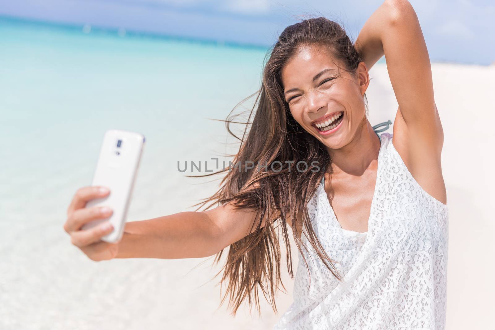 Selfie summer beach vacation fun girl laughing. Happy Asian woman taking self-portrait pictures with mobile phone on tropical holidays in Caribbean posing for camera.