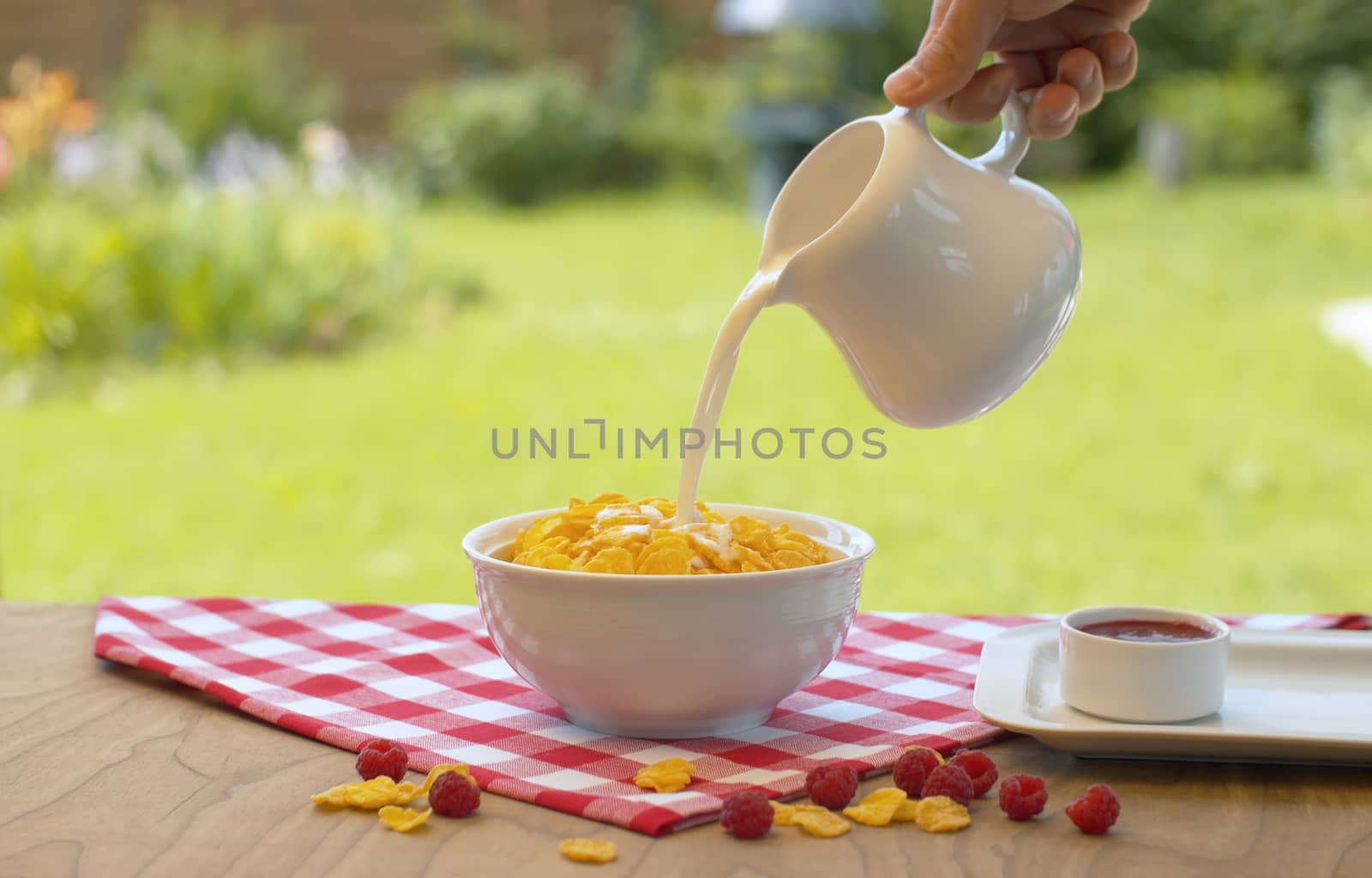 Close up male hand pouring milk into the bowl with cornflakes. Unrecognizable man cooking breakfast in the garden. Healthy lifestyle concept