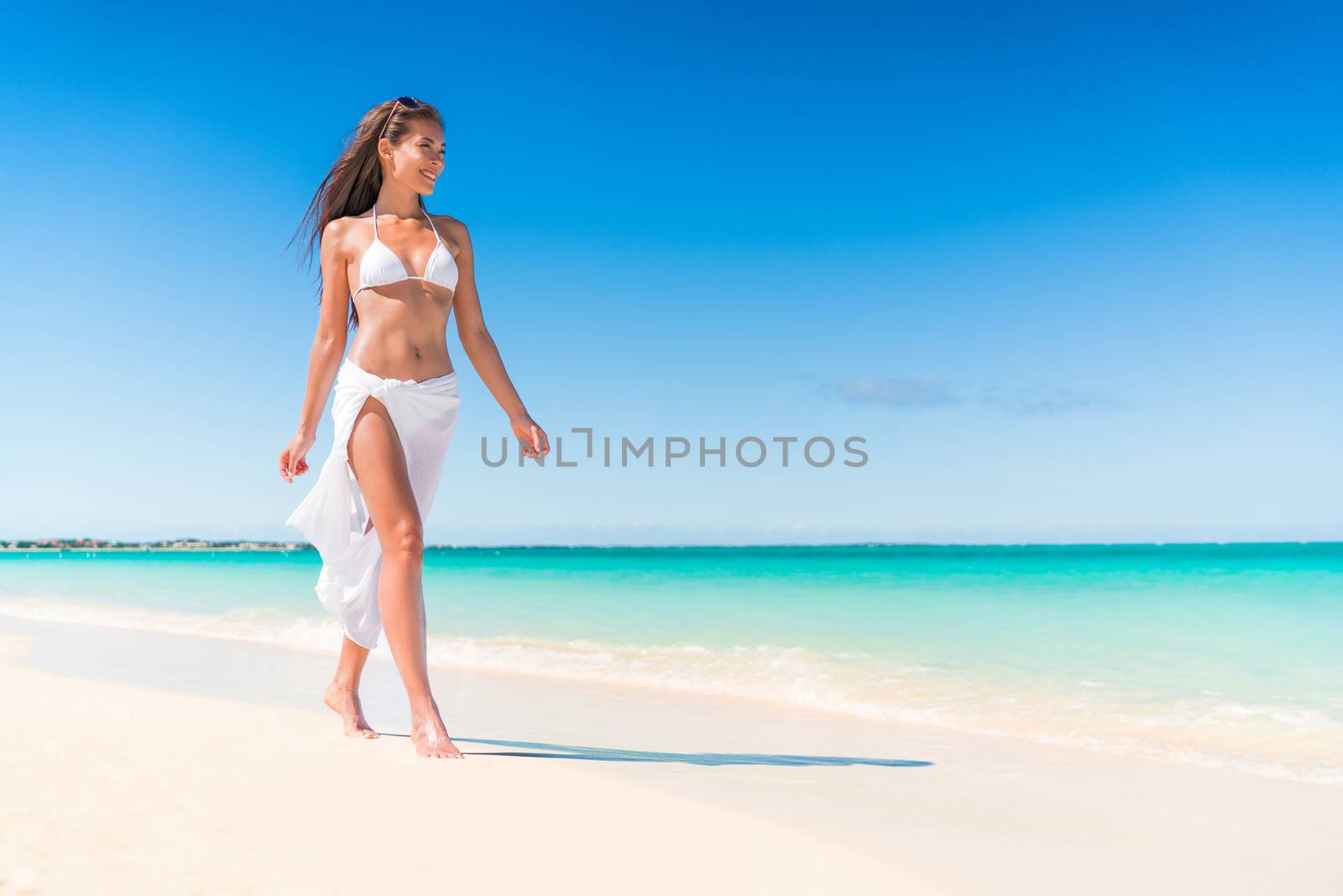 Luxury beach travel vacation swimwear woman relaxing walking on white sand in beachwear cover-up. Asian girl on tropical destination paradise wearing pareo fashion swimwear.