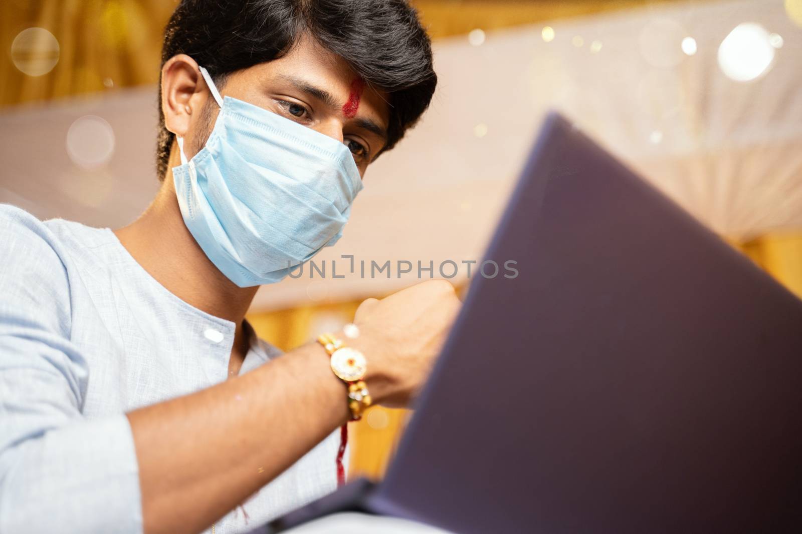 young man with medical mask making video call and showing Rakhi or Raksha Bandhan to his sister or family friends after festival ceremony during coronavirus ot covid-19 pandemic