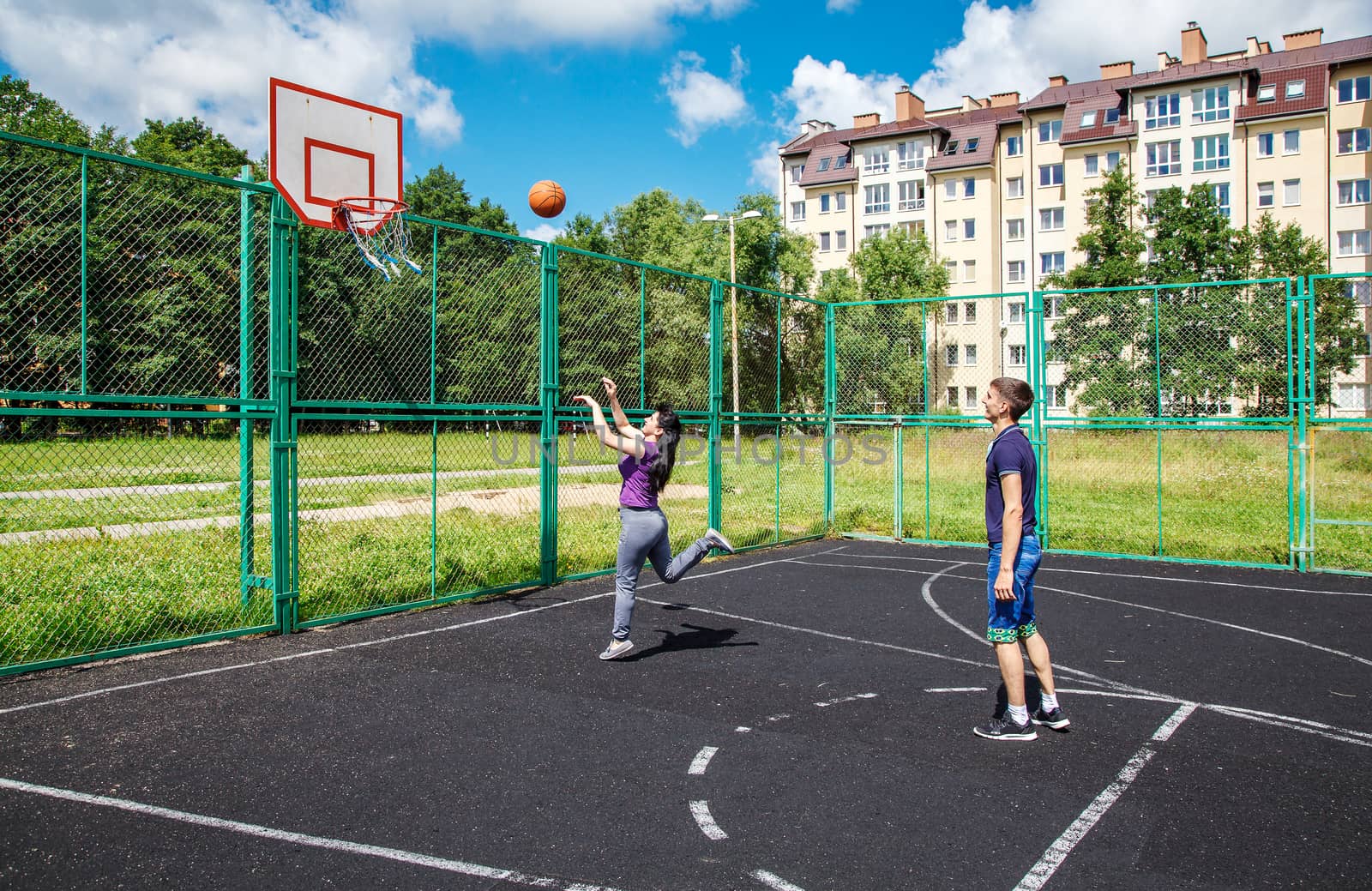 young man playing basketball with his mother on the sports groun by raddnatt