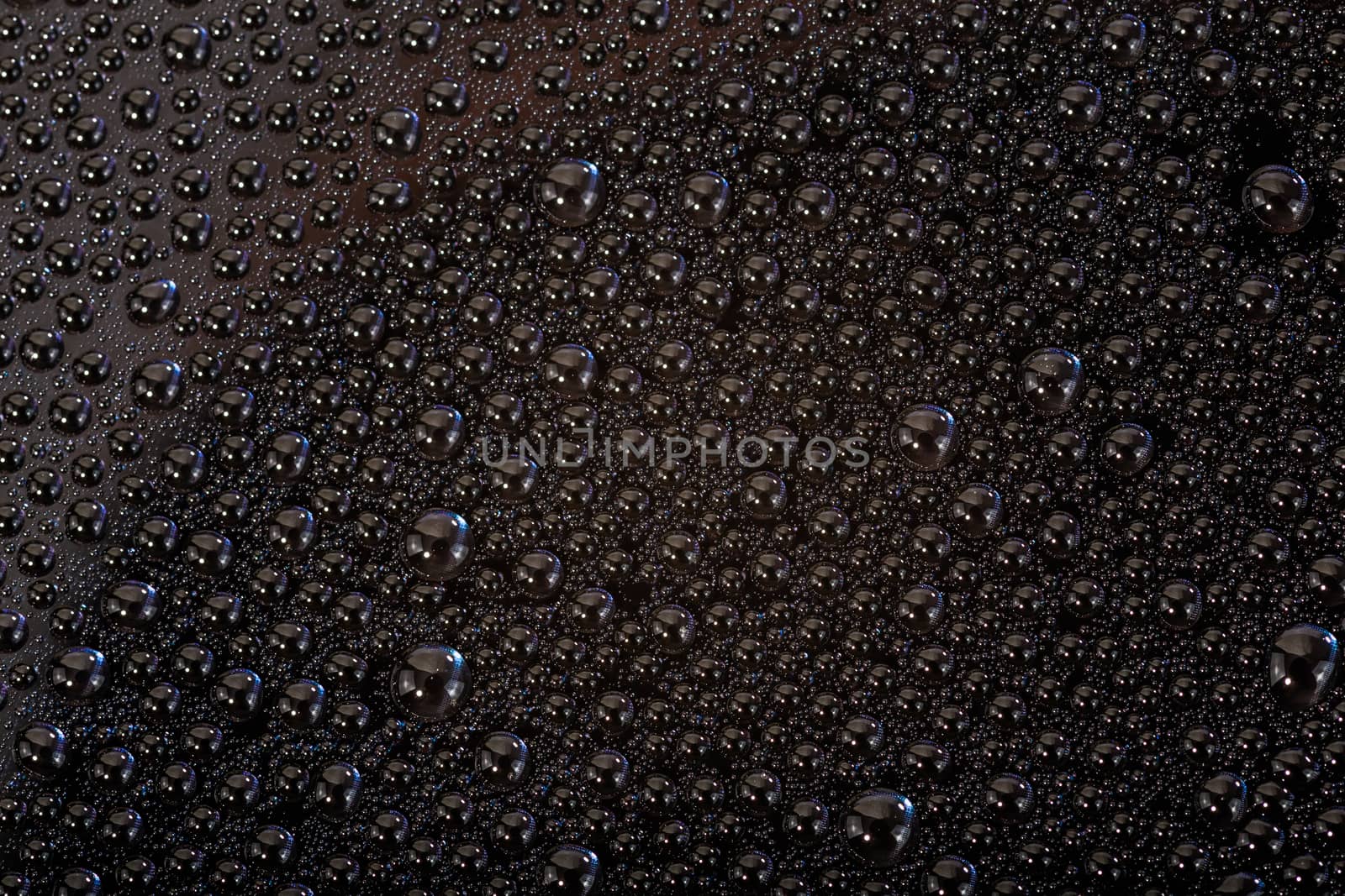 many small water drops on the black surface of cellphone hydriphobic coated glass screen, close-up with selective focus and visible subpixel rgb triads