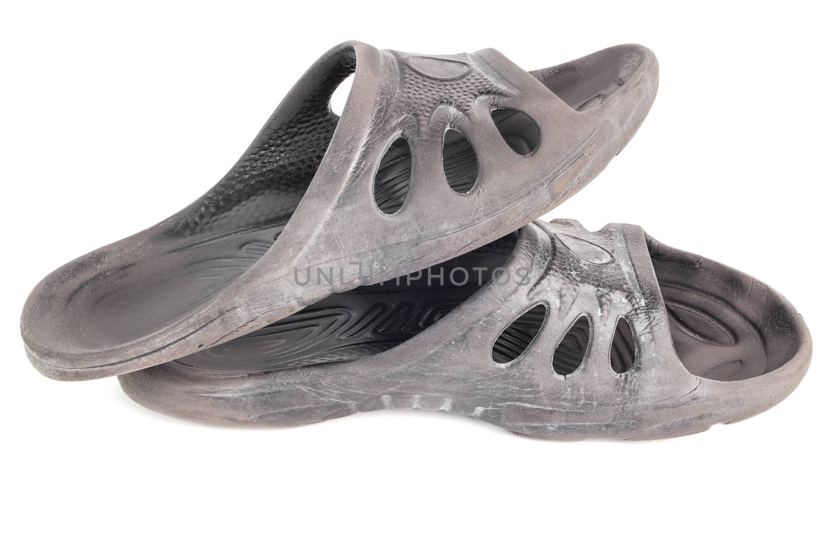 pair of used cheap black soft rubber slippers with signs od friction wear isolated on white background.