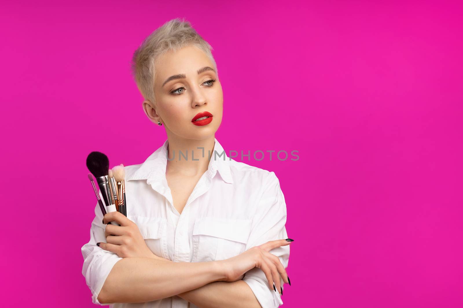Close up portrait makeup artist. Make up courses. Concept of self visage masterclasess. Fashion professional. Woman hold makeup brushes on the hands. Studio shot on the pinkcolor background