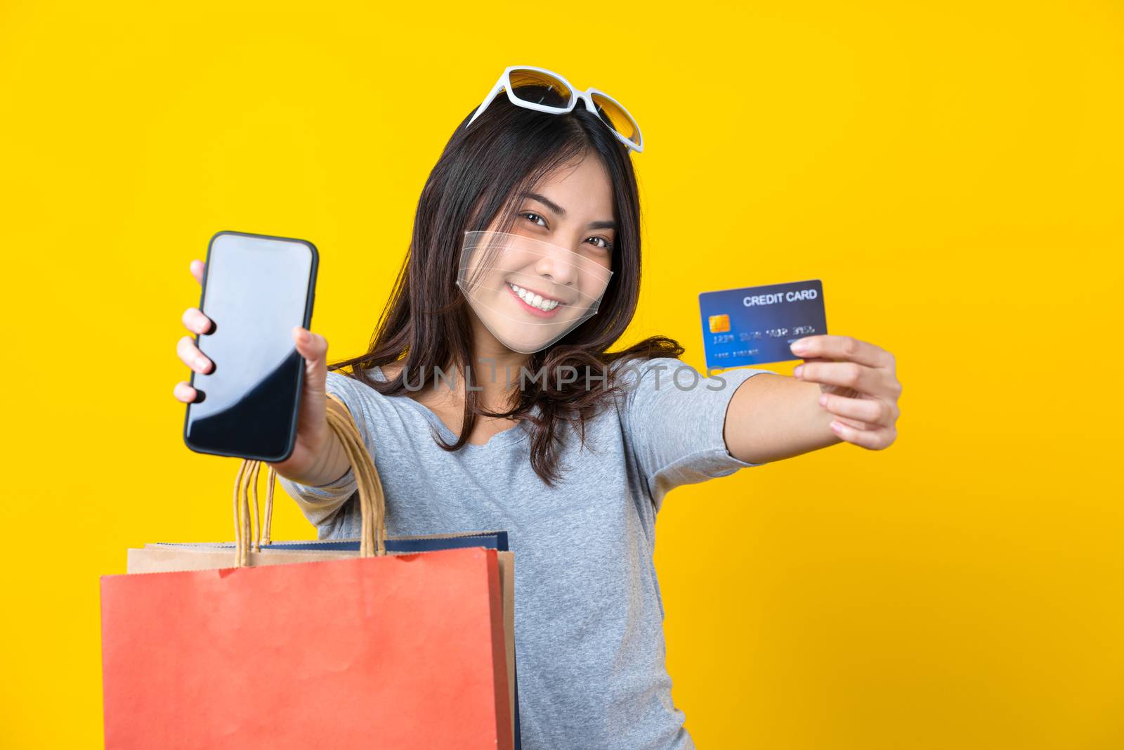 Happy Asian smiling woman wearing technology augmented reality surgical mask in covid19 outbreak  and presenting credit card and mobile phone with Carrying a shopping colorful bag for online shopping