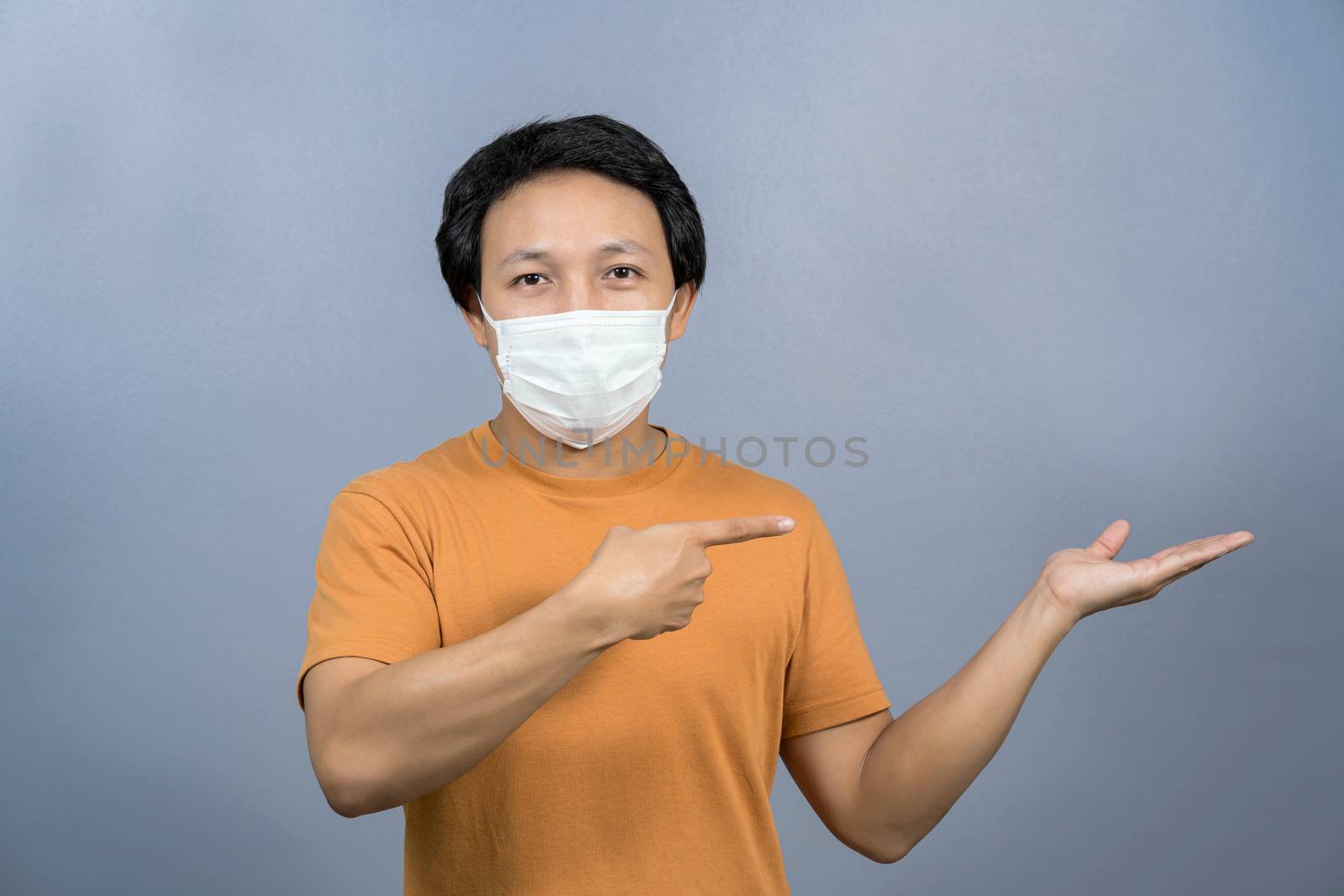 Asian man wearing face surgical mask pointing and presenting som by Tzido