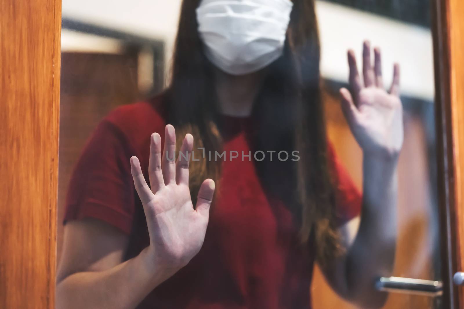 Closeup hand of Asian woman wearing medical mask touching Glass door when stay isolation at home for self quarantine in Covid19 outbreak situation,coronavirus pandemic and lockdown,Low light situation