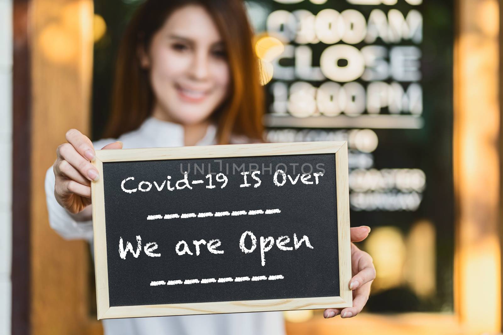 Closeup Asian partner Small business owner hands holding and showing the chalkboard with wording Covid-19 is over and we are open sign in front of coffee shop,new normal after Covid gone, coronavirus