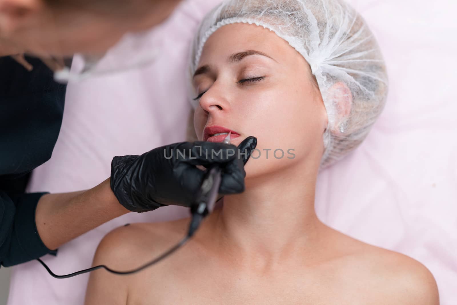 Cosmetology cabinet client lies on couch. Beautician applies marking on lips. Preparation for the procedure of permanent lips makeup. Close up. Beauty industry