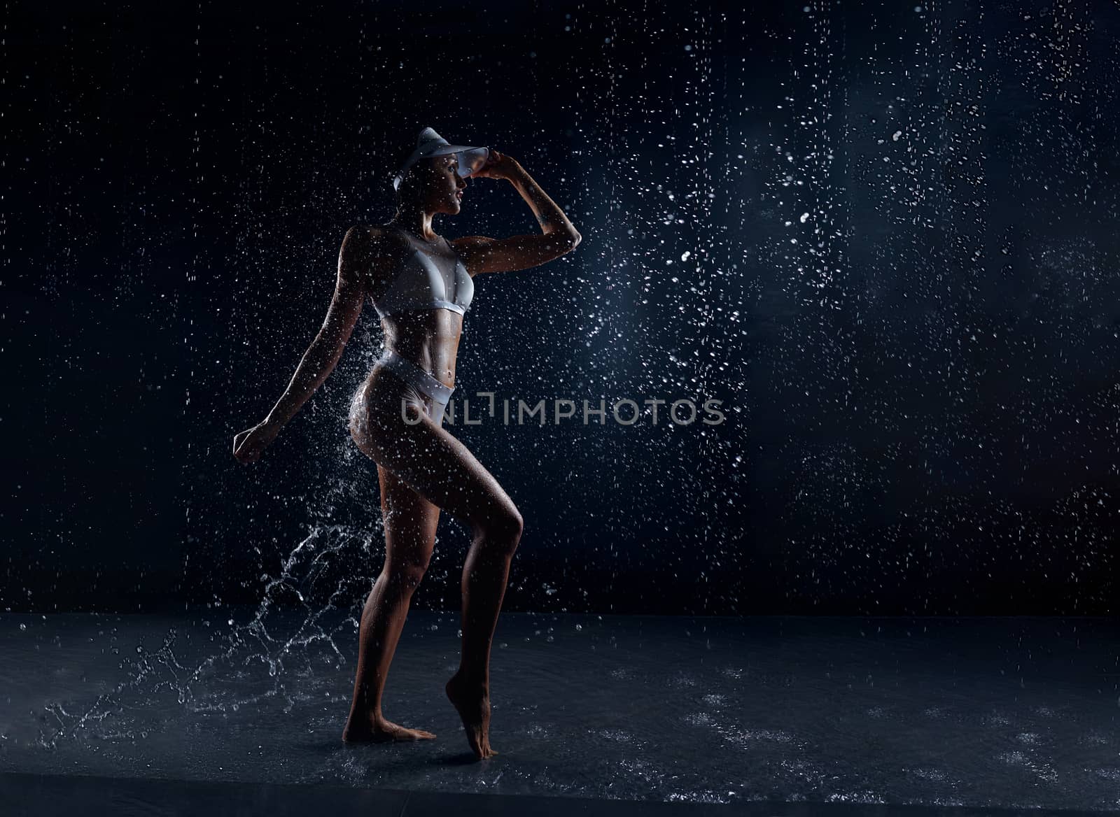 Beautiful athletic caucasian girl with a perfect figure is standing under the water. Fitness woman in a spray of water. Sports freshness. concept by andreonegin