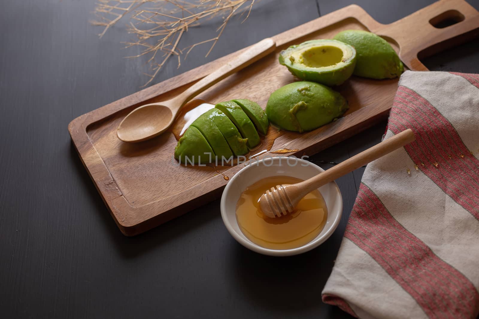 Fresh organic avocado sliced in half and honey on black wooden table.