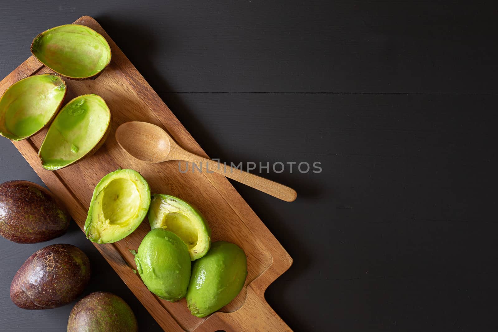 Fresh organic avocado sliced in half on black wooden table by kaiskynet