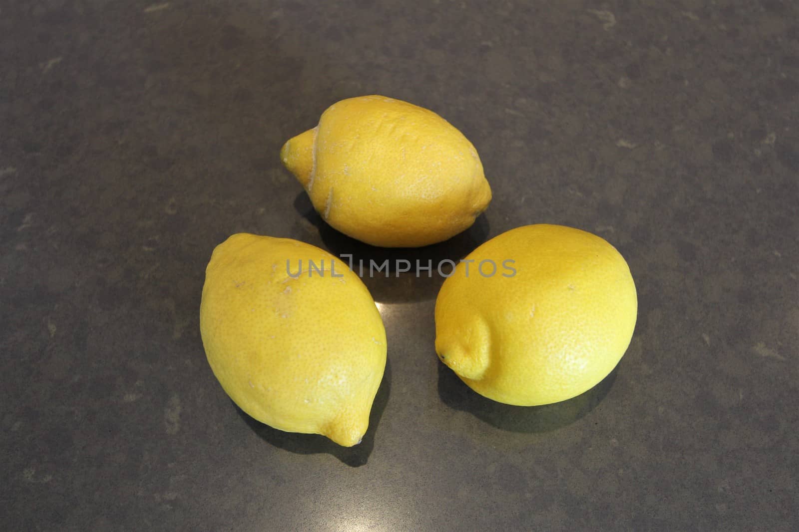 Three whole yellow lemons on a gray stone surface