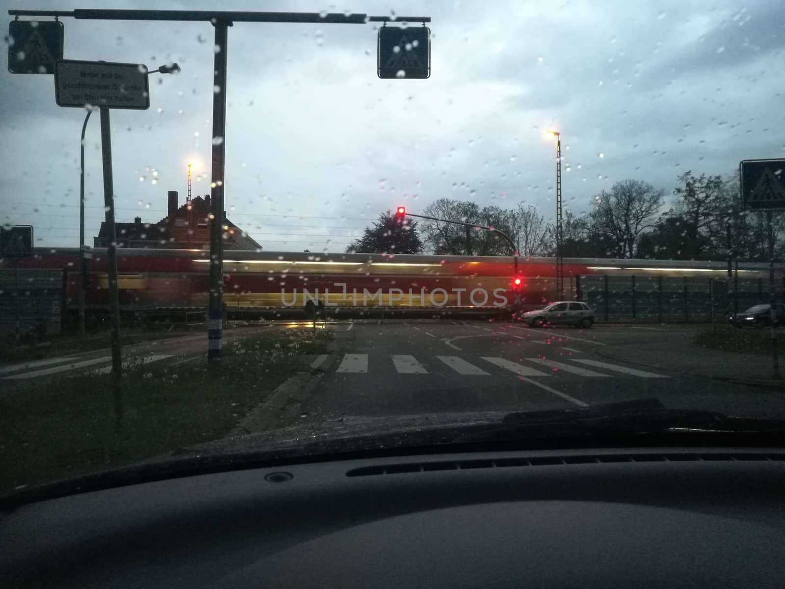 Closed barriers of a railroadcrossing at dusk in the rain while a train passes by