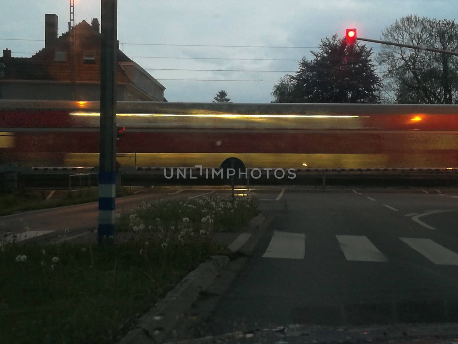 Closed barriers of a railroadcrossing at dusk in the rain while a train passes by