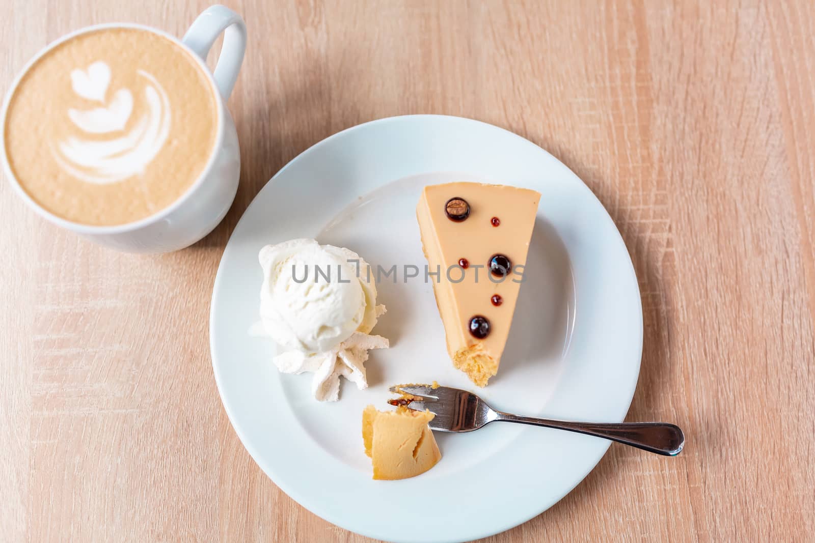 A piece of caramel cheesecake served with ice cream and a cup of cafe latte, flat lay