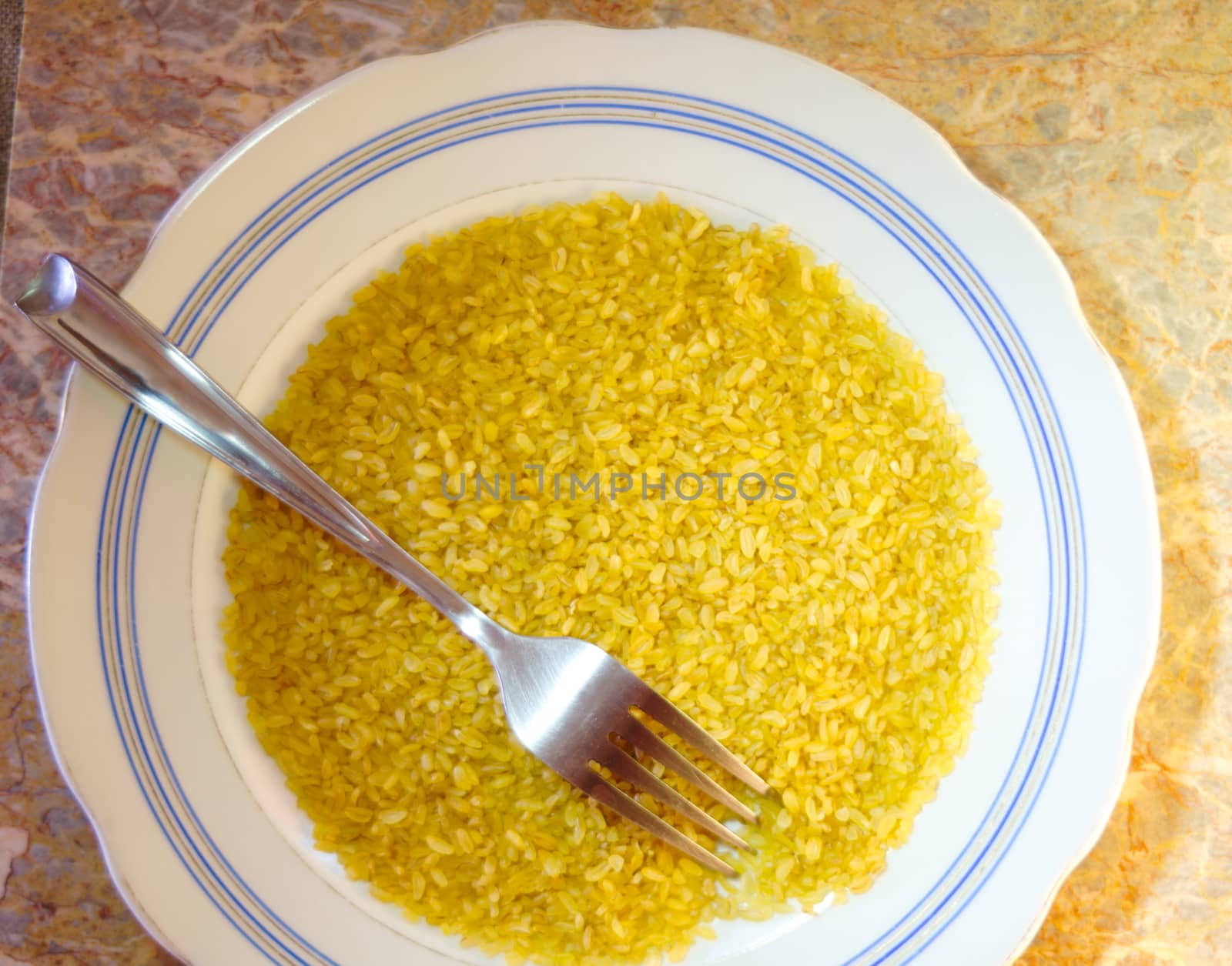 top view of a white plate with a round edging of stripes, on a plate bulgur porridge and a fork for food, background - marble