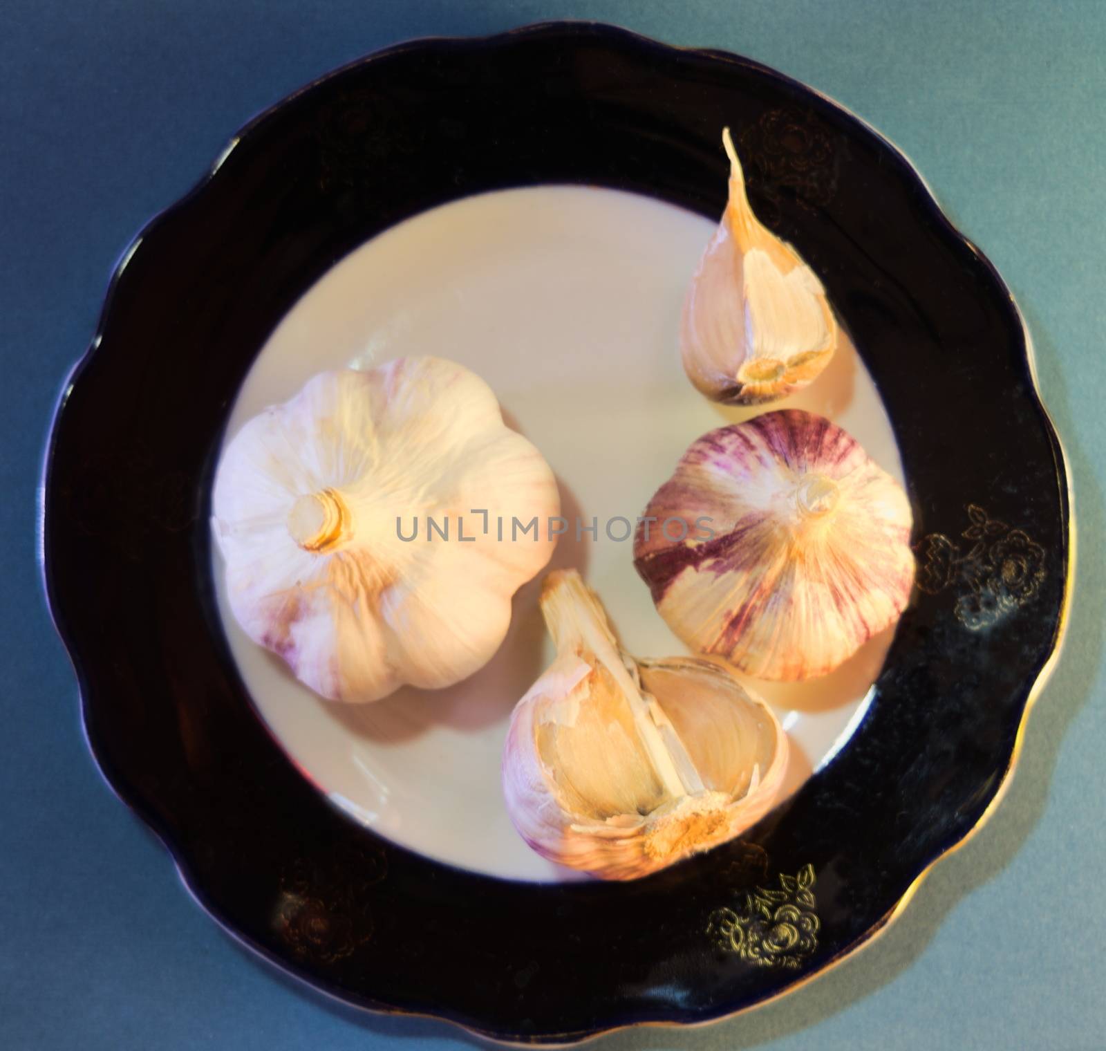 top view of a composition of young garlic heads on a black and white plate, background - blue