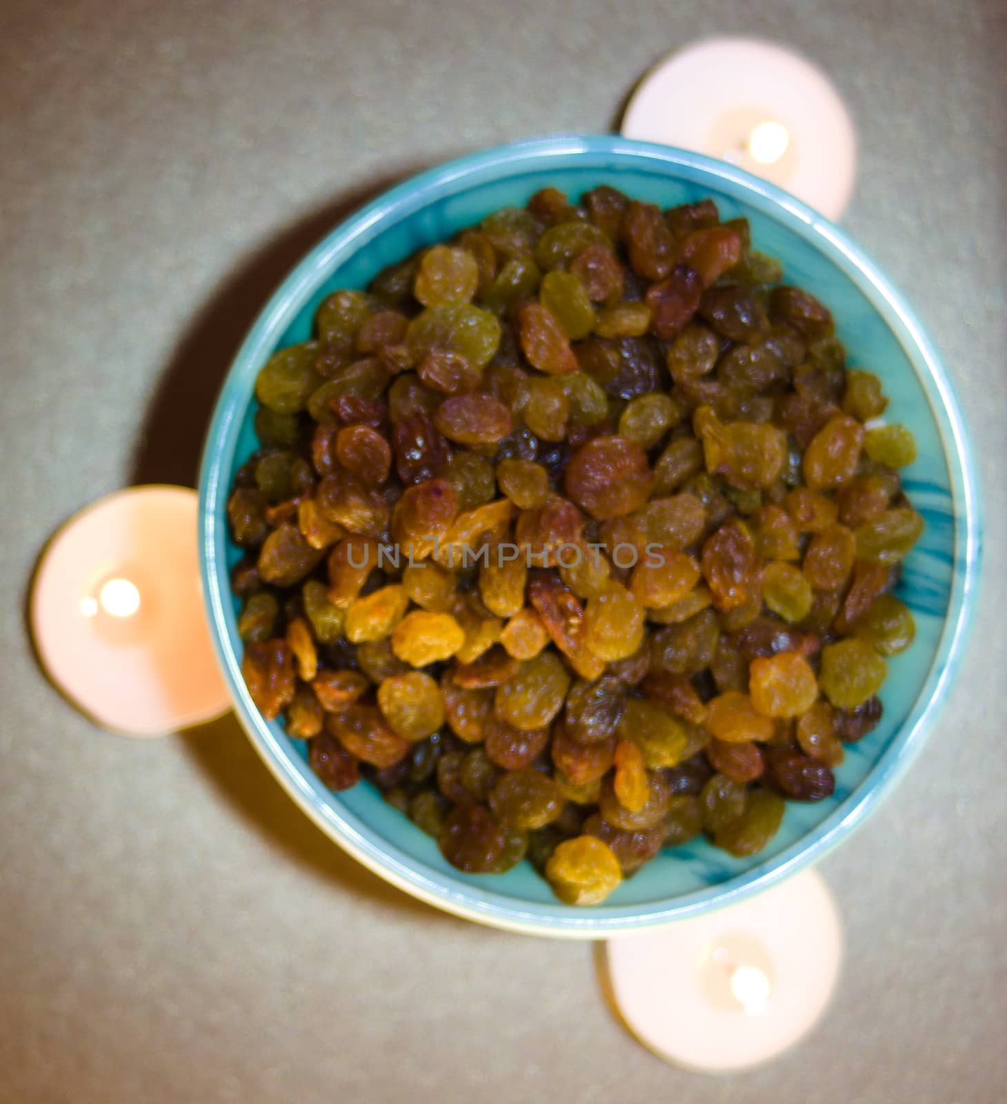 top view of a green plate with raisins on a light background with the light of a flame of burning candles
