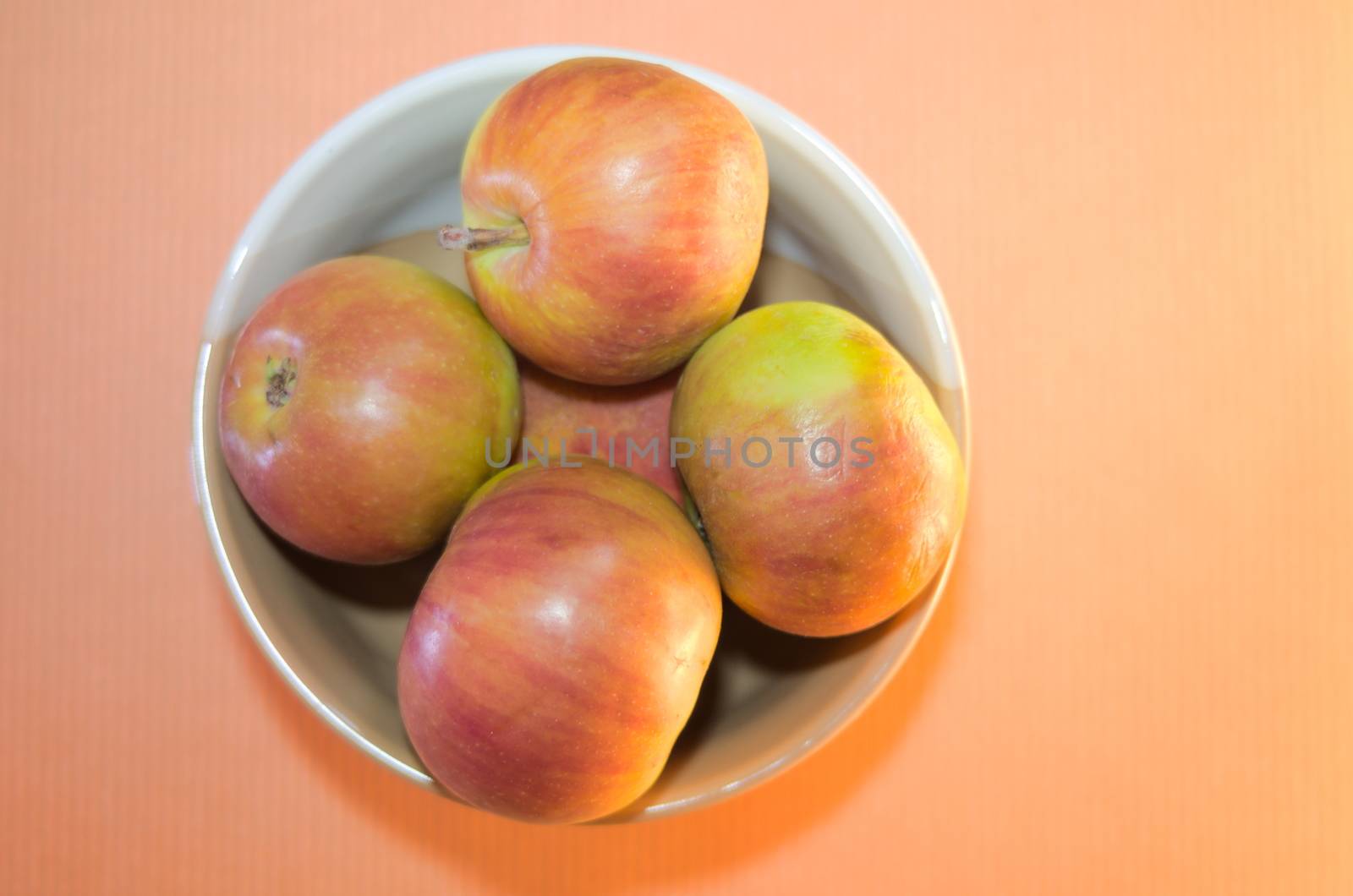 red-yellow summer apples in a light bowl on a pink background close-up top view