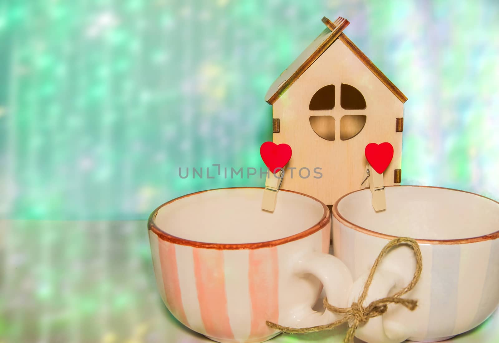 Two cups in blue and pink, tied with rope, red clothespins with hearts and a wooden house. The concept of a strong family with a copy of the space felt hearts.