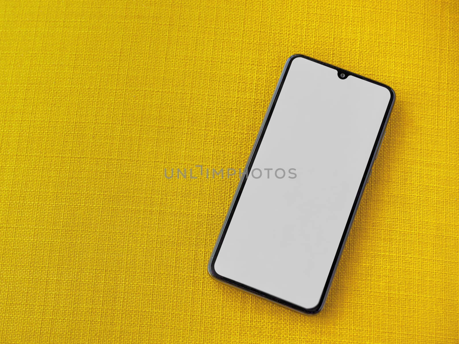 Black mobile smartphone mockup lies on the surface with a blank screen isolated on a yellow fabric background. Top view close up with selective focus and copy space.