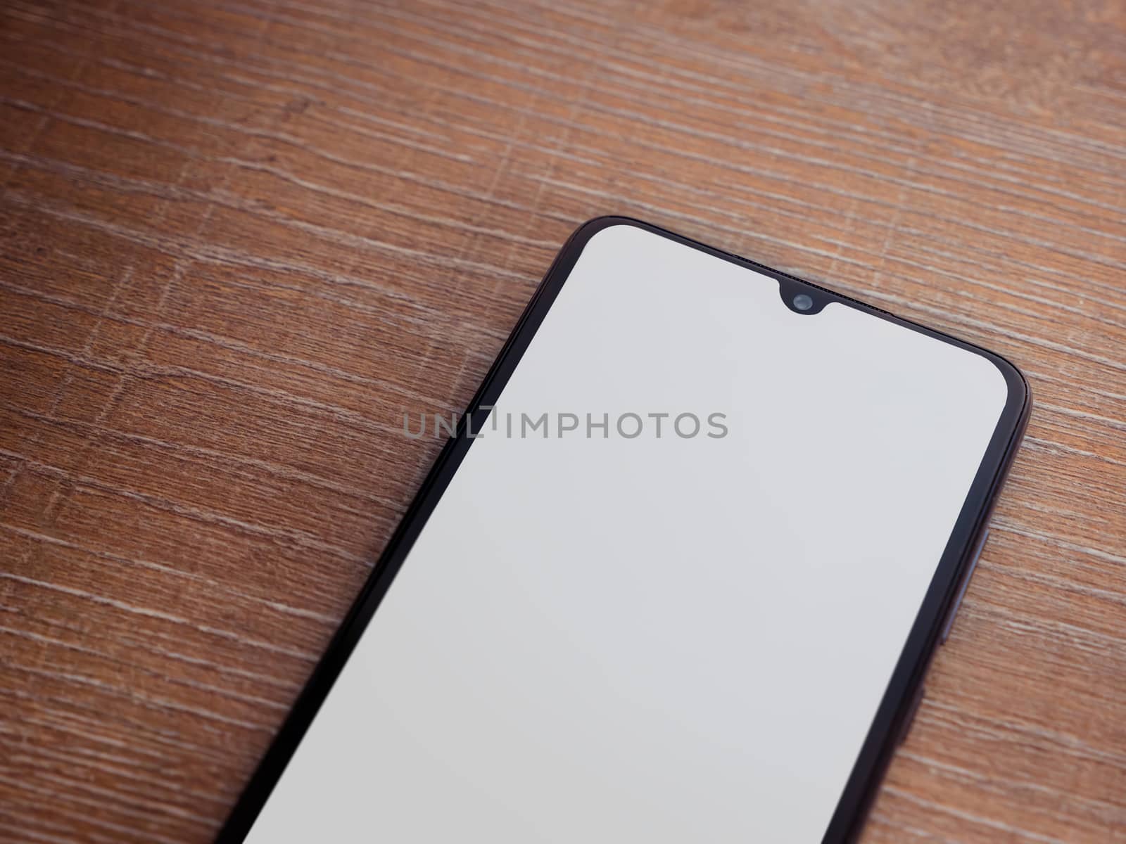 Black mobile smartphone mockup lies on the surface with blank screen isolated on wooden background. Top view closeup with selective focus and copy space, cut in the middle.