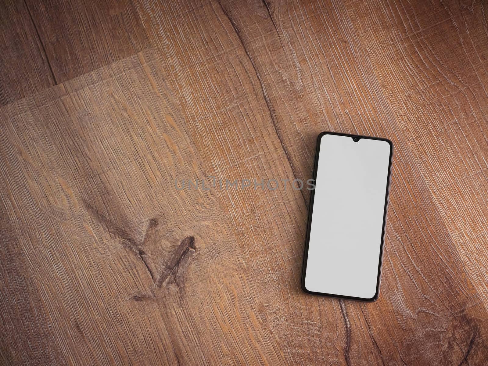 Black mobile smartphone mockup lies on the surface with blank screen isolated on wooden background. Top view flat lay with copy space.
