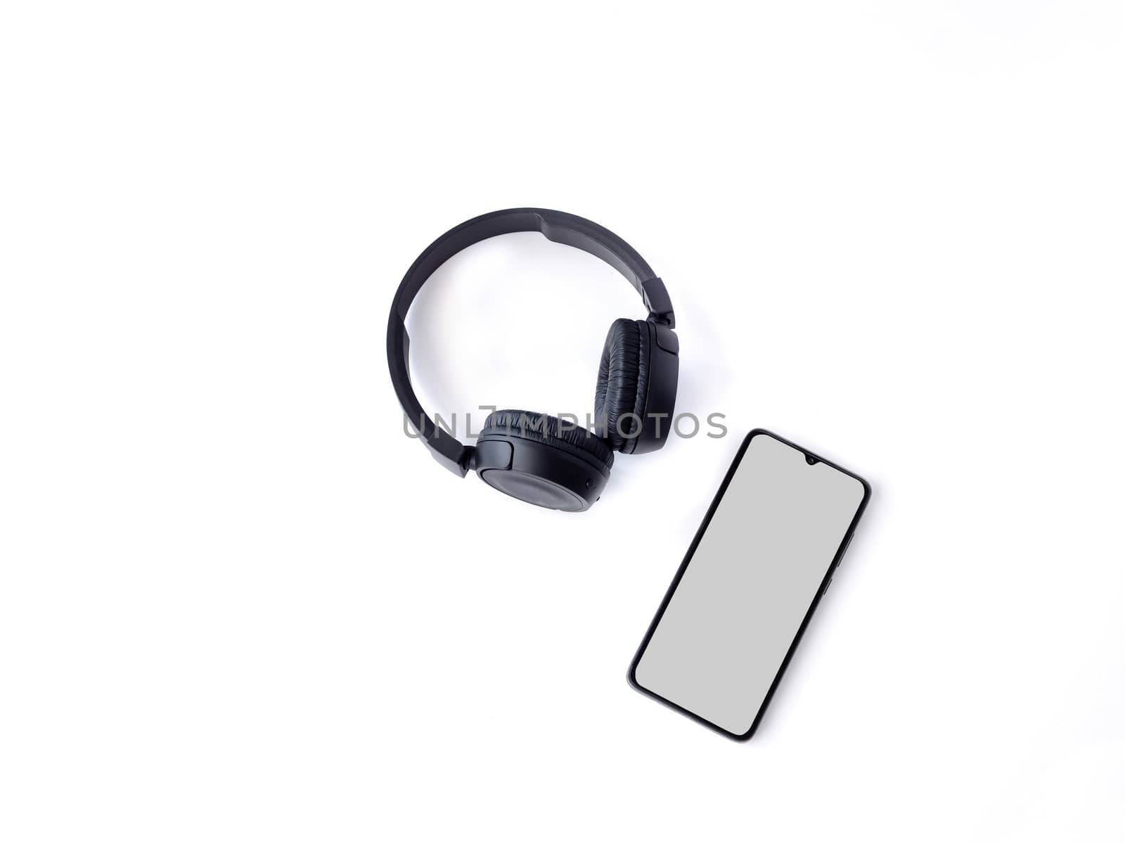 Black wireless headphone and mobile smartphone with a blank screen mockup lay on the surface of a white background by wavemovies