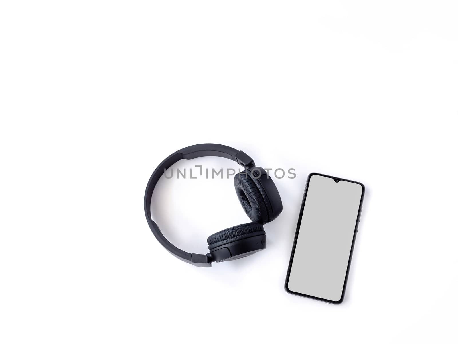 Black wireless headphone and mobile smartphone with a blank screen mockup lay on the surface of a white background by wavemovies