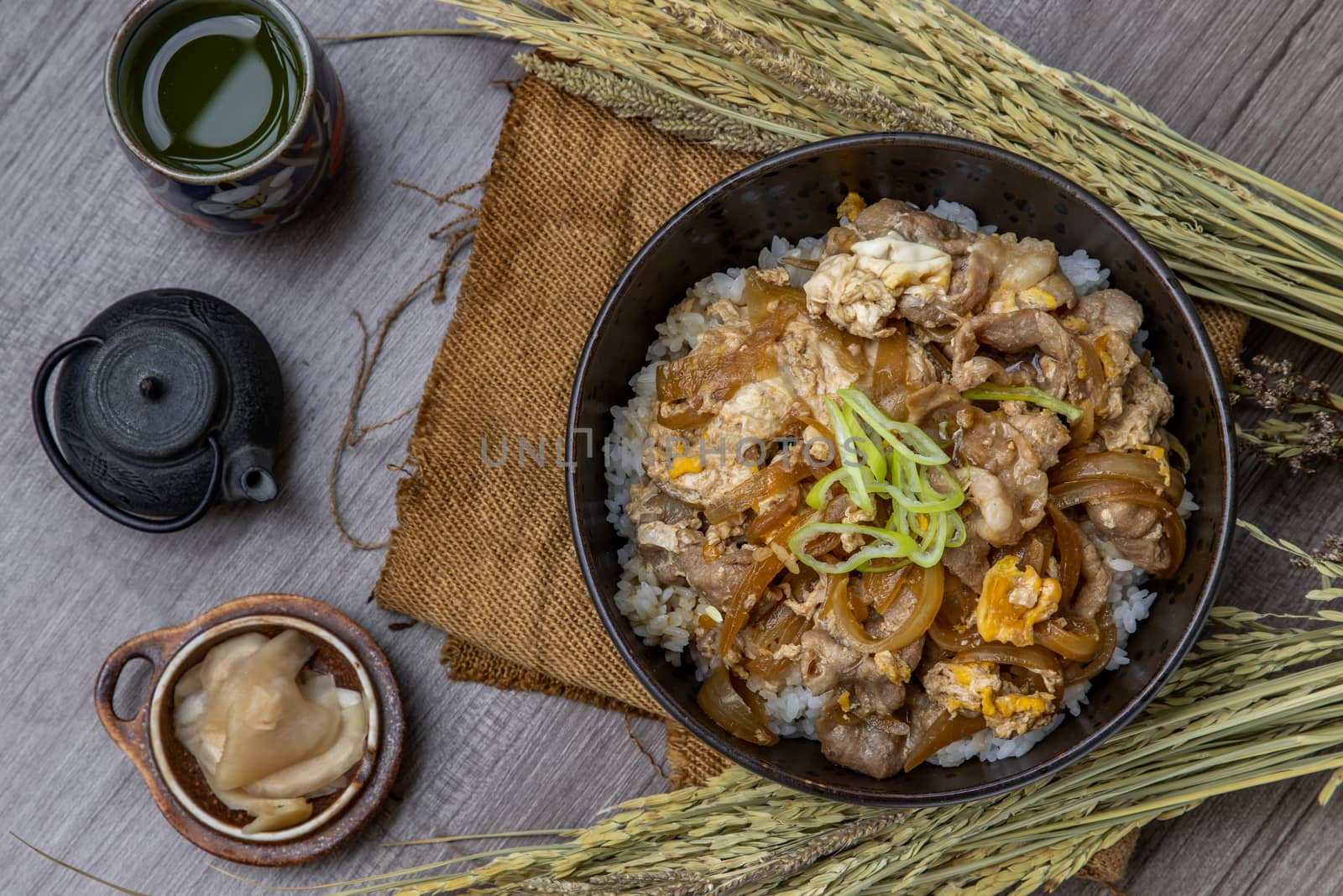 Japanese pork rice bowl with egg and onion (Donburi) served with pickled ginger and green tea on wooden table. Japanese food style.