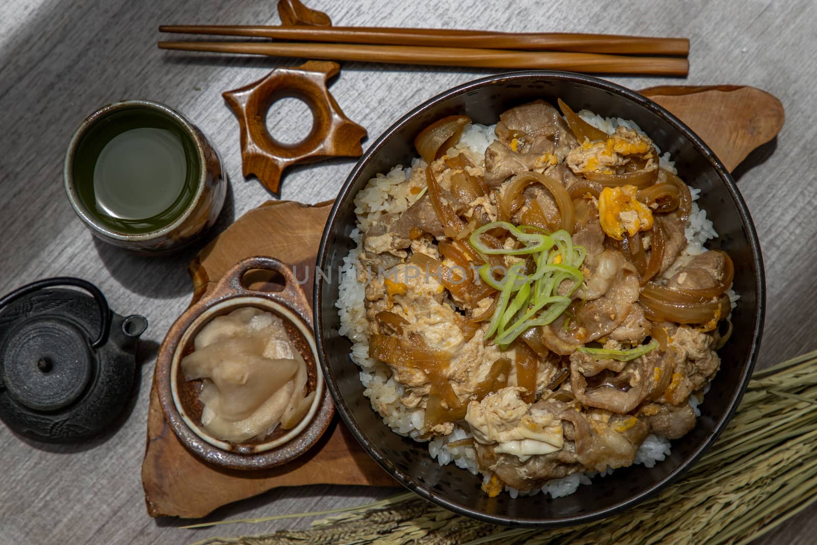 Japanese pork rice bowl with egg and onion (Donburi) served with pickled ginger and green tea on wooden table. Japanese food style.