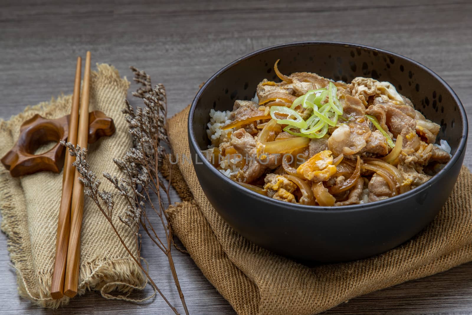 Japanese pork rice bowl with egg and onion (Donburi) served with pickled ginger and green tea on wooden table. Japanese food style.