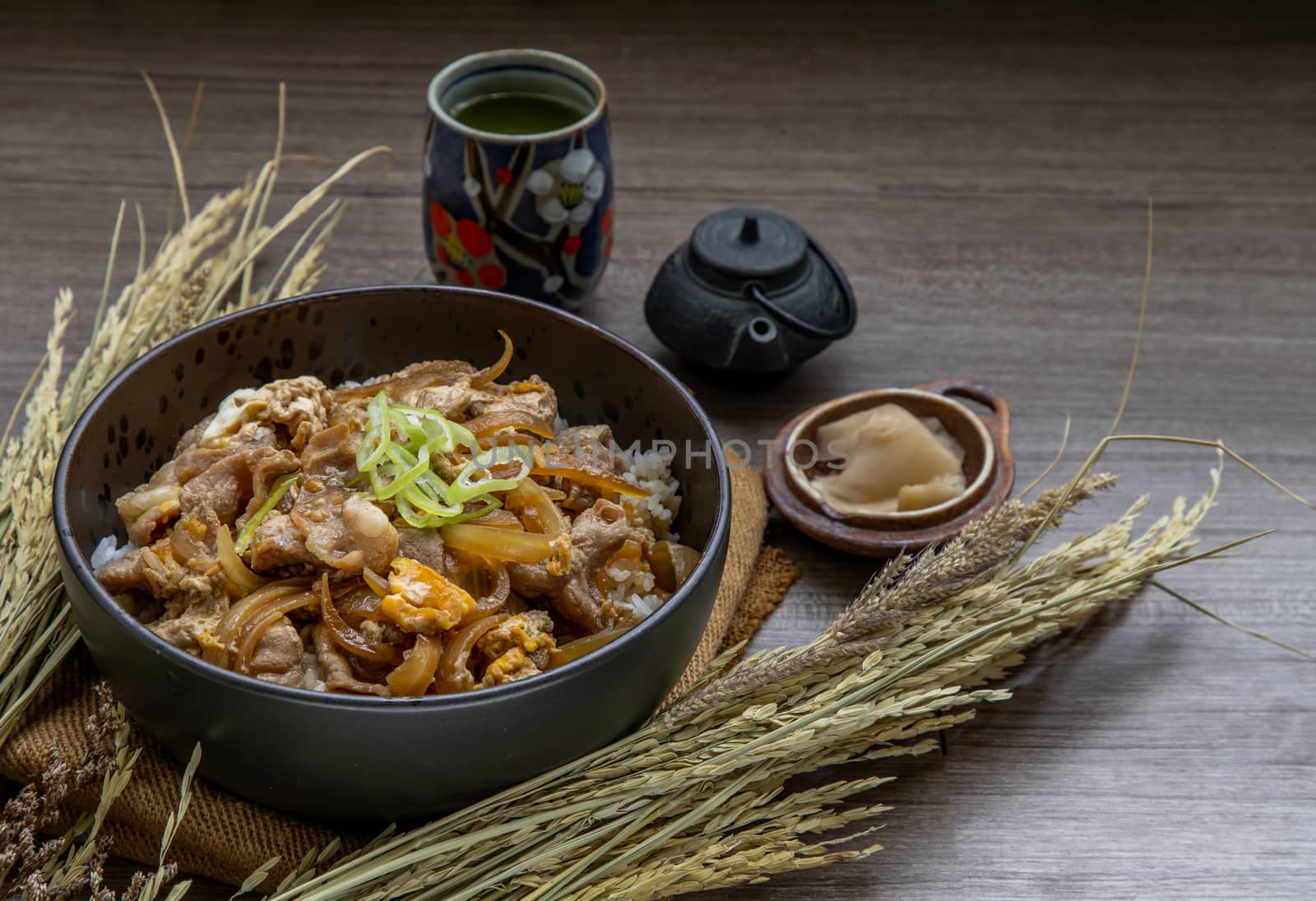 Japanese pork rice bowl with egg and onion (Donburi) served with pickled ginger and green tea on wooden table. Japanese food style.