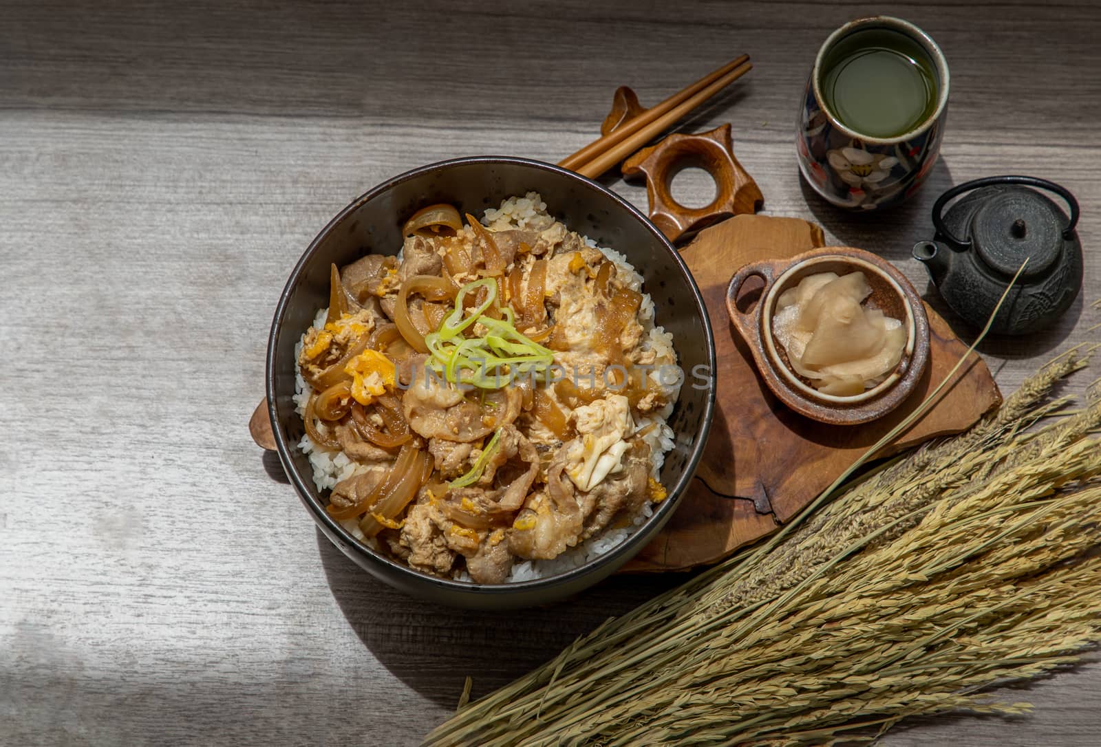 Japanese pork rice bowl with egg and onion (Donburi) served with pickled ginger and green tea on wooden table. Japanese food style.