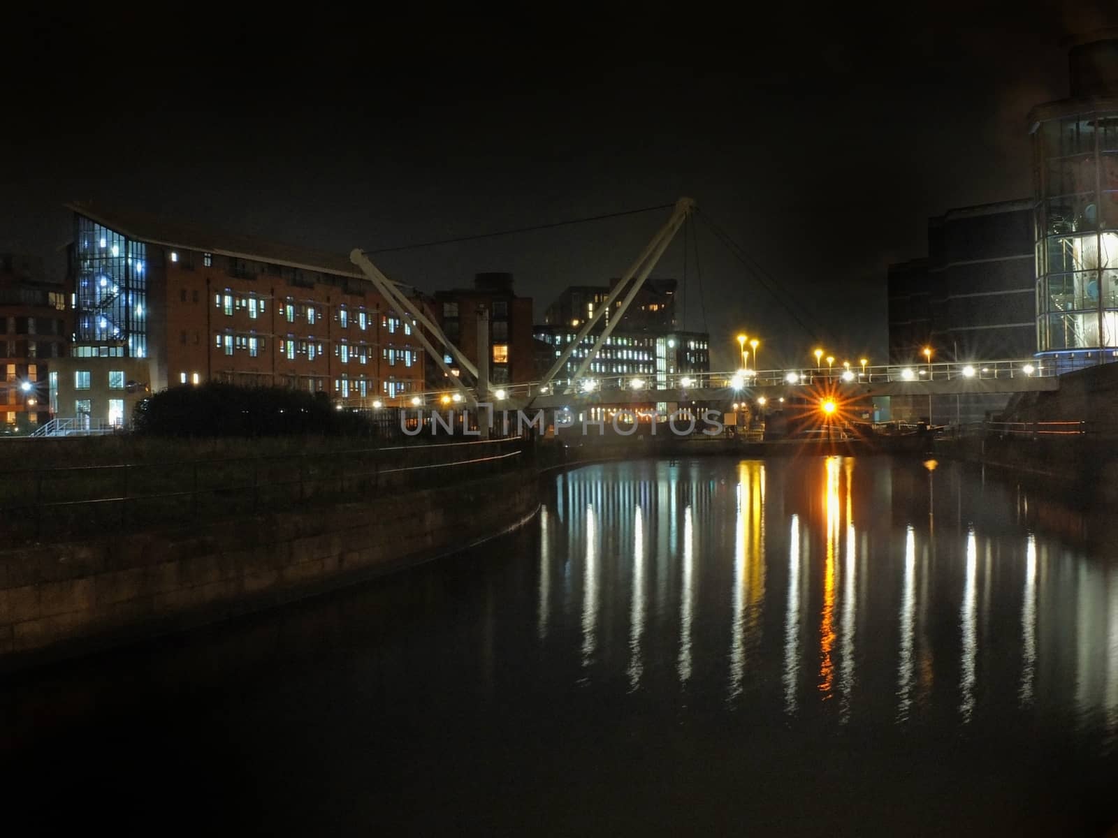 Knights Way Footbridge crossing the river aire at the lock entrance to clarence dock in leeds at night with buildings and lights reflected in the water