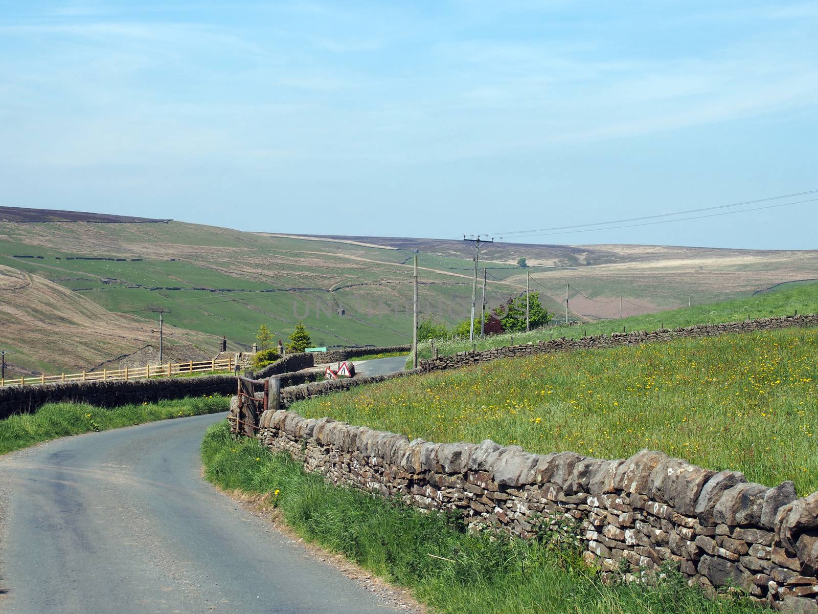 a narrow country lane surrounded by dy stone walls in a sunlit rural hilly landscape on the old howarth road in calderdale west yorkshire