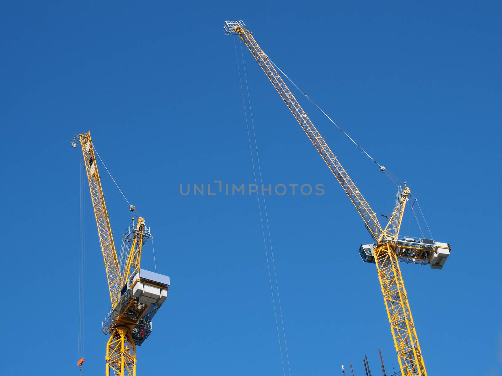 two tall yellow tower cranes working on a construction site against a blue sky