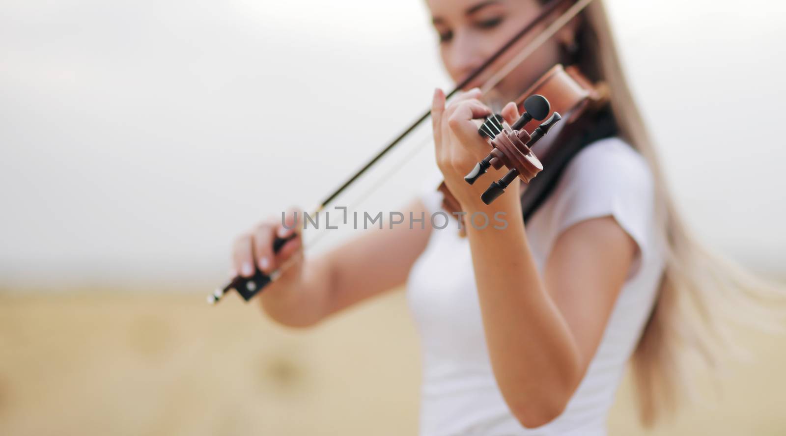 Beautiful romantic girl with loose hair playing the violin in the field after the harvest. Square sheaves of hay in the field. Violin training