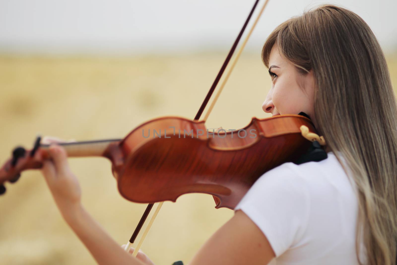 Beautiful romantic girl with loose hair playing the violin in the field after the harvest. Square sheaves of hay in the field. Violin training