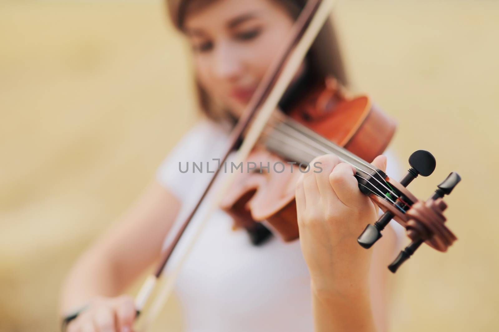 Beautiful romantic girl with loose hair playing the violin in the field. by selinsmo