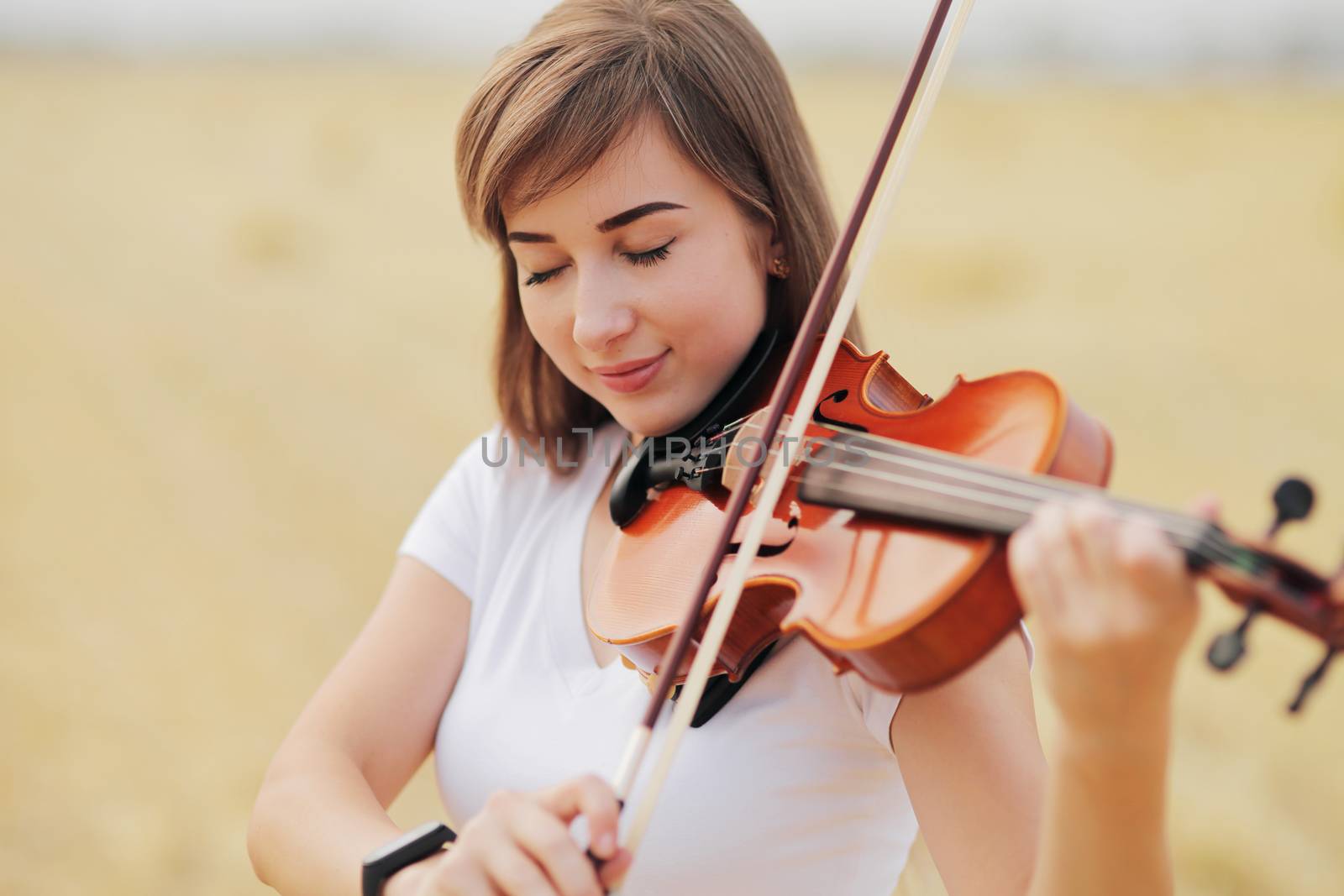 Beautiful romantic girl with loose hair playing the violin in the field. by selinsmo