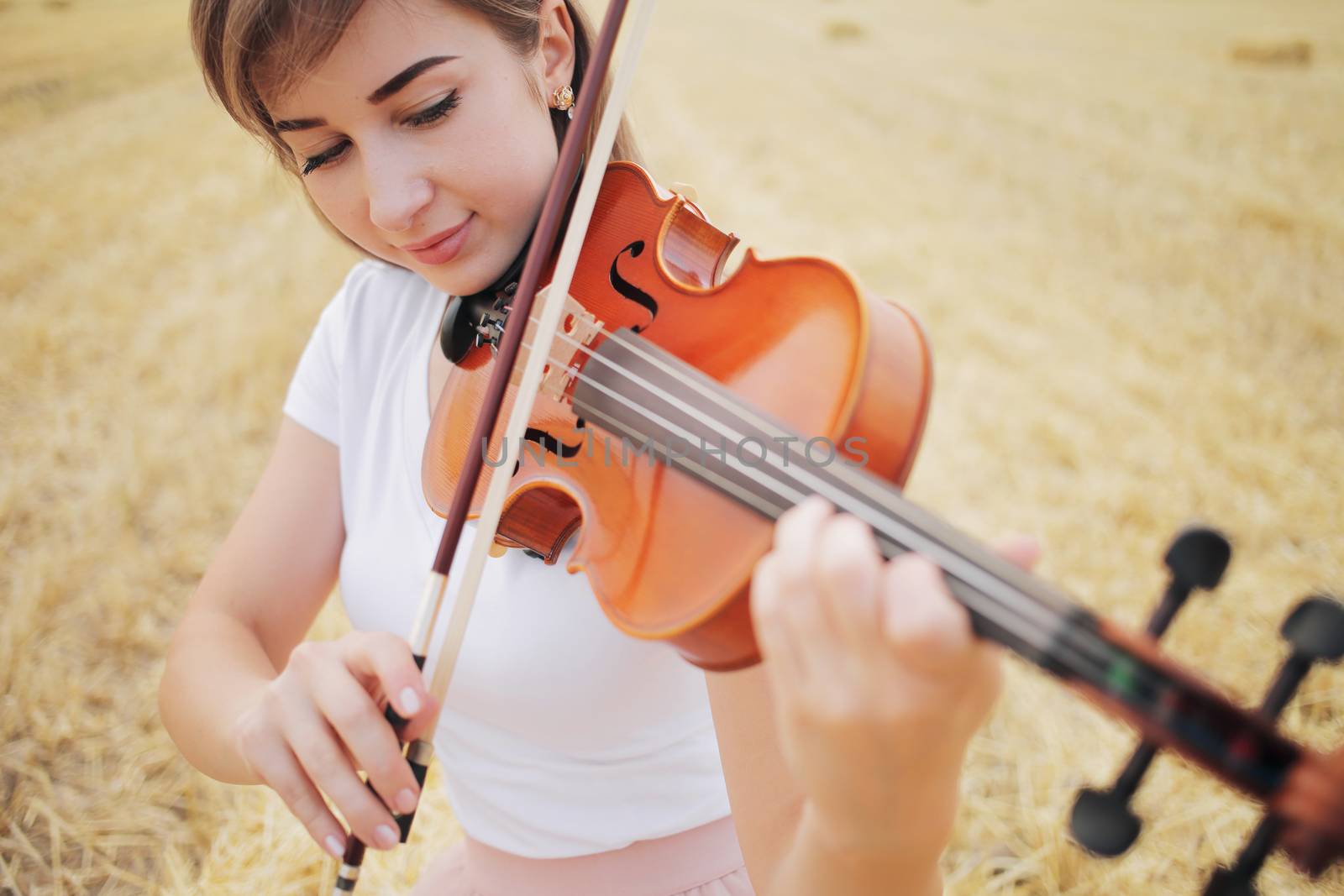 Beautiful romantic girl with loose hair playing the violin in the field. by selinsmo